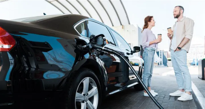 Photograph of a young woman at a gas station, fueling up her car.